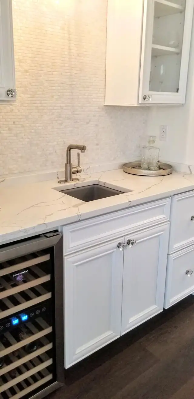 Wet bar with white quartz countertop, square stainless bar sink, brushed faucet and white cabinets above a wine cooler