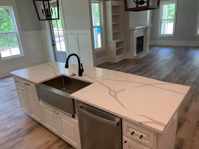 White kitchen island with gray-veined quartz top, stainless farmhouse sink and dark faucet